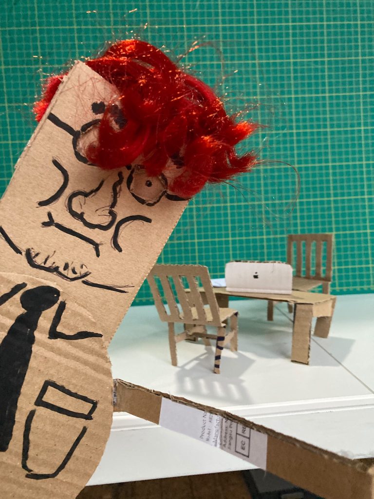 A cardboard puppet in a miniature cardboard office at DoES Liverpool